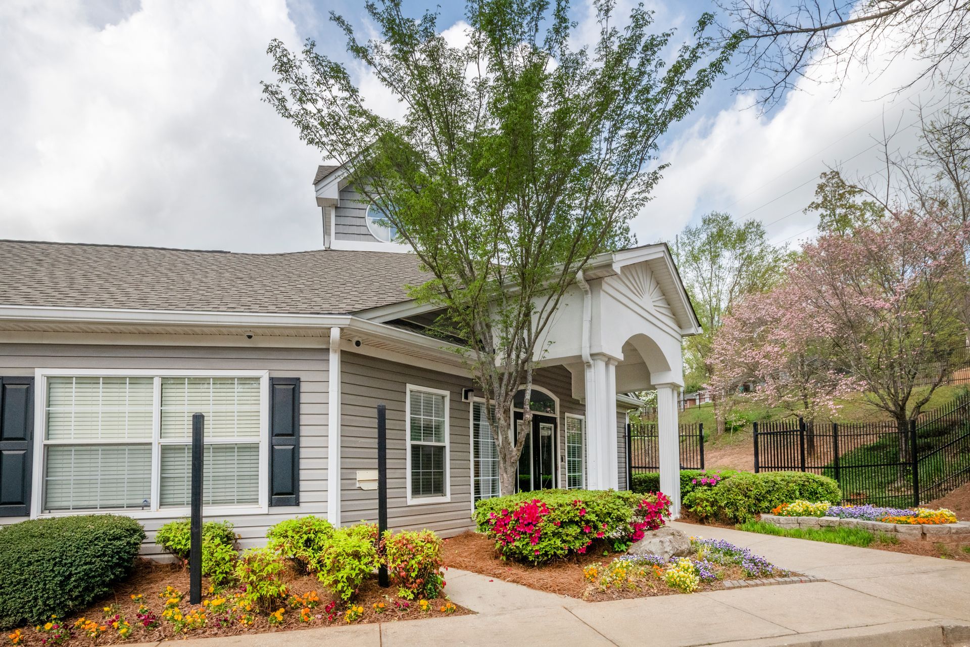 Suburban house with front porch, white siding, black shutters, and colorful flower beds