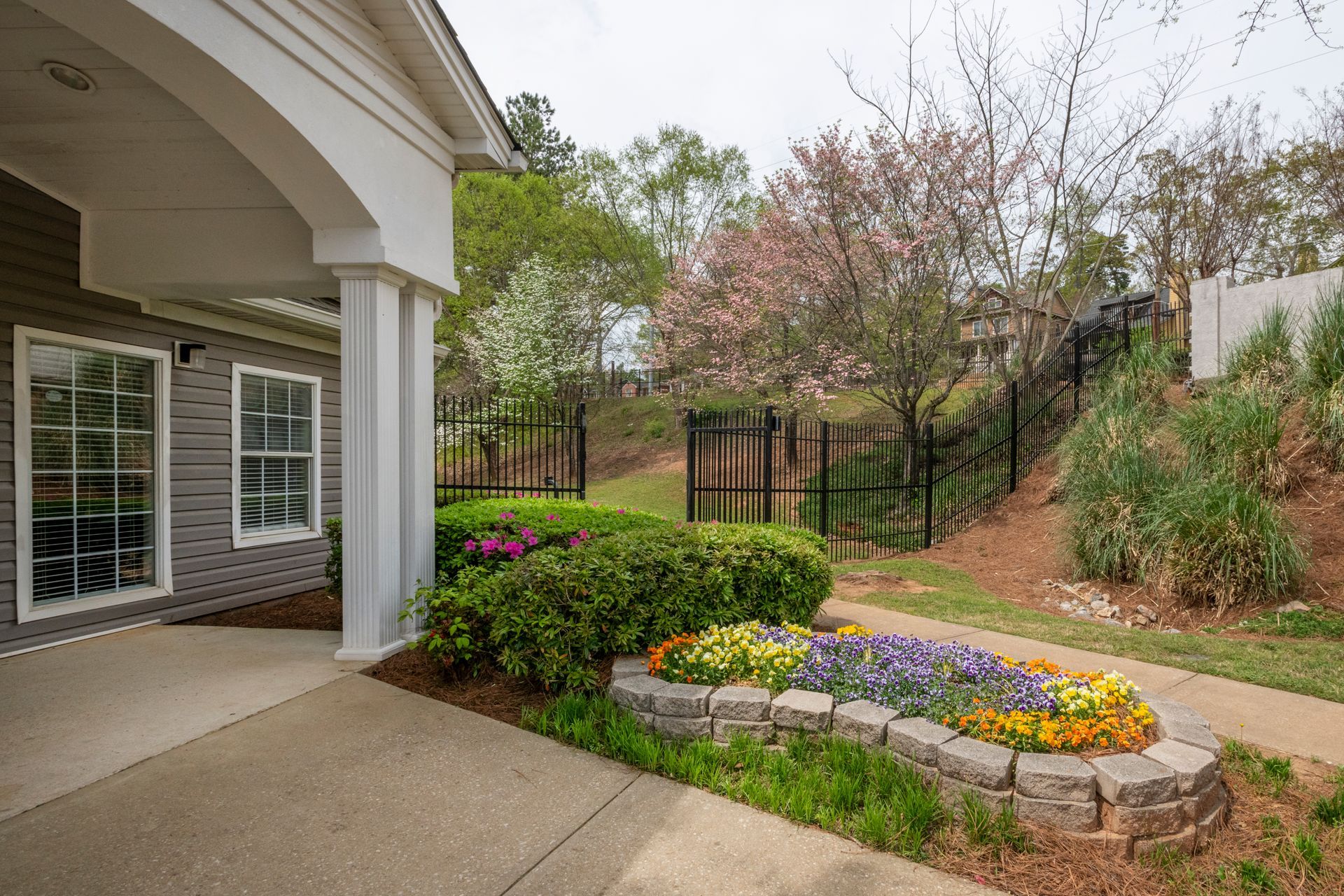 Covered patio beside landscaped garden with colorful flowers, shrubs, and a tree-lined yard.