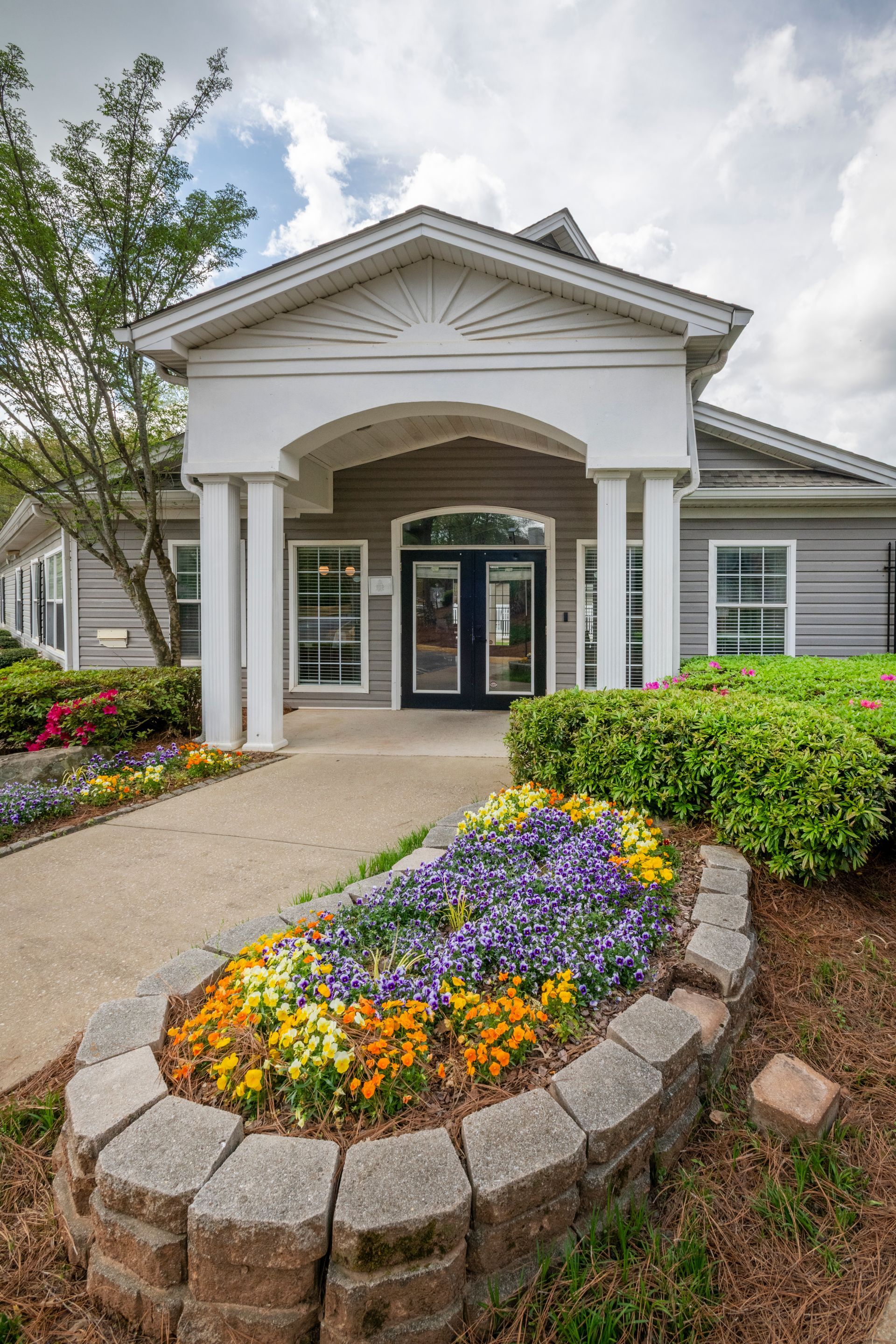 Entrance of a white building with columns, glass doors, and a flower bed in front