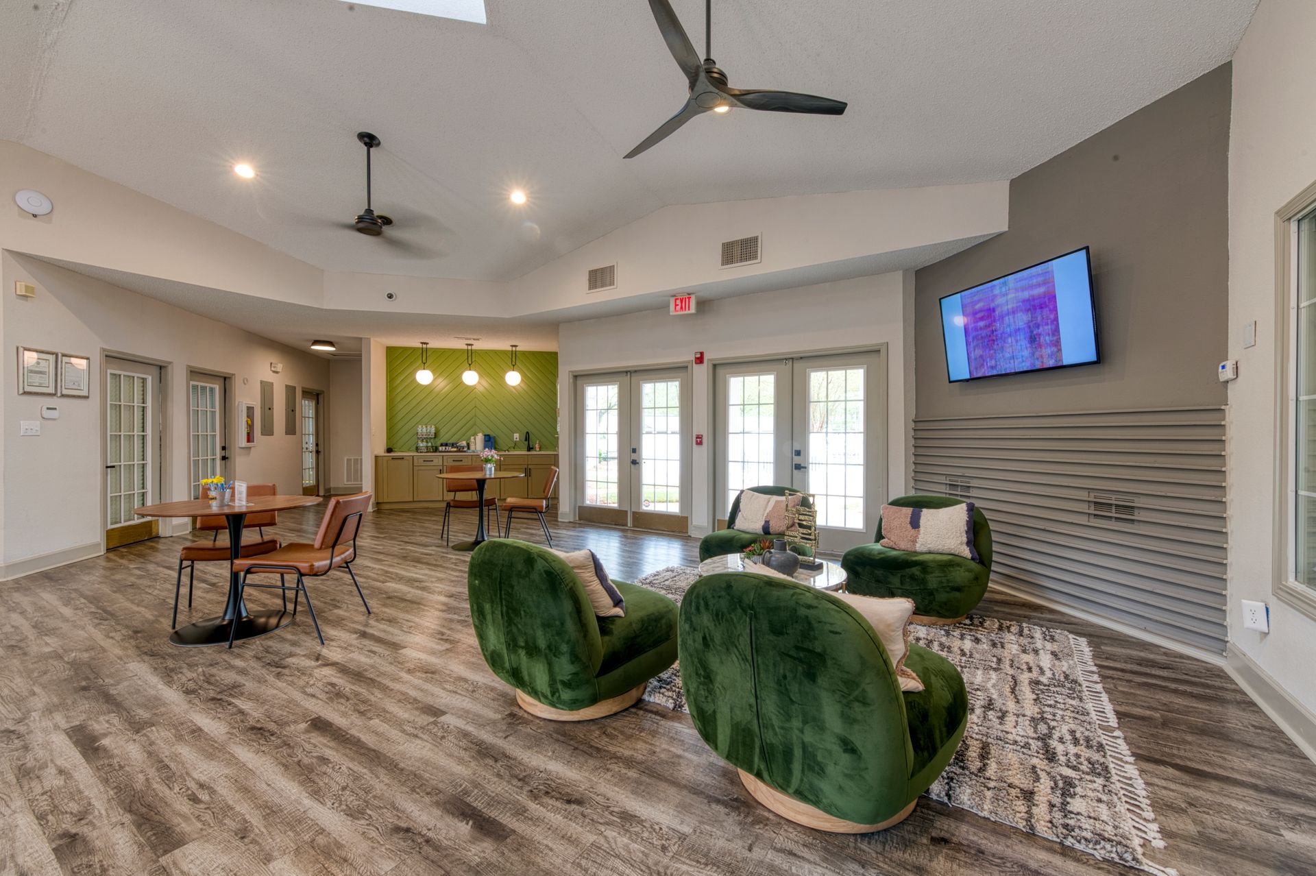 Modern lobby with green chairs, wood flooring, ceiling fans, and wall-mounted TV