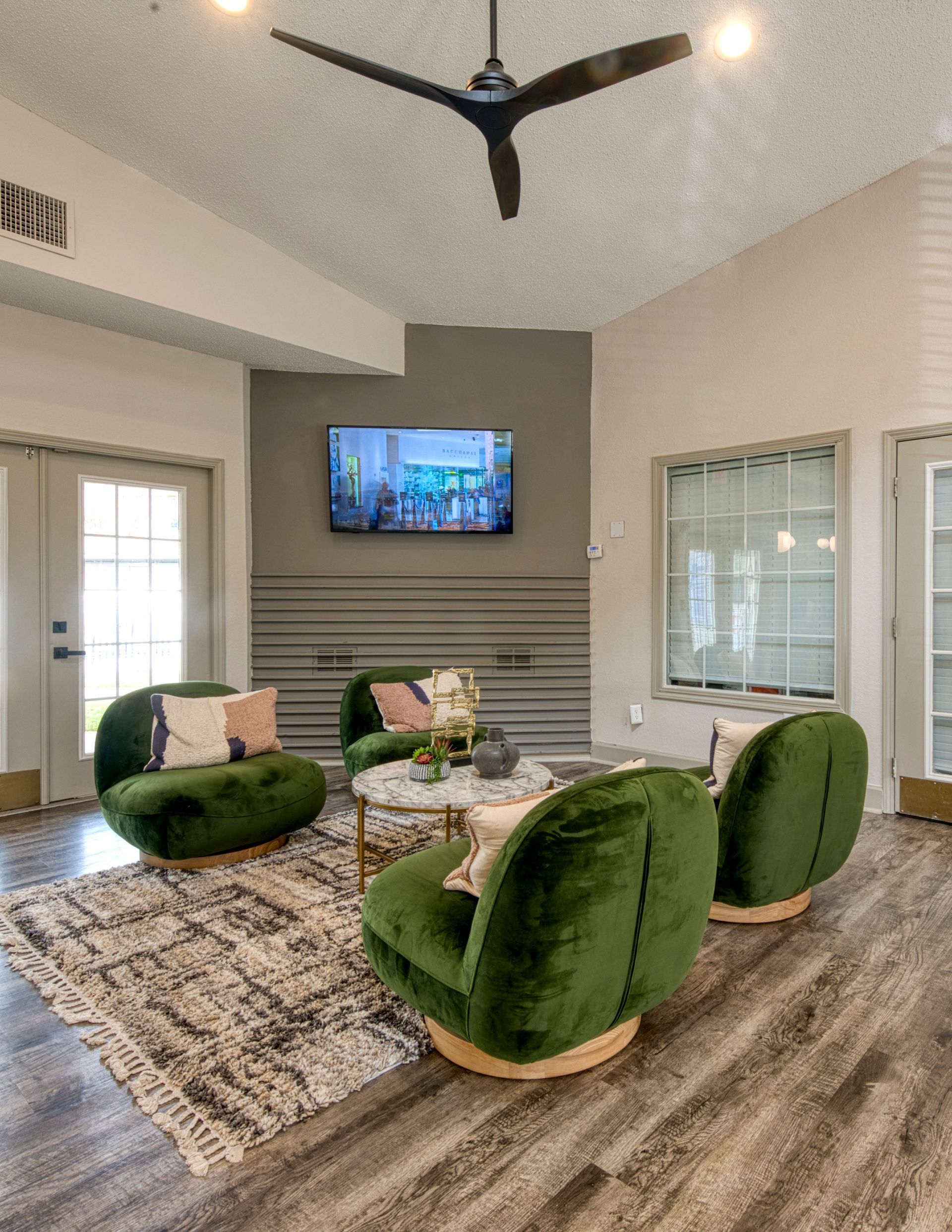 Modern living room with green chairs, wall-mounted TV, striped rug, and ceiling fan