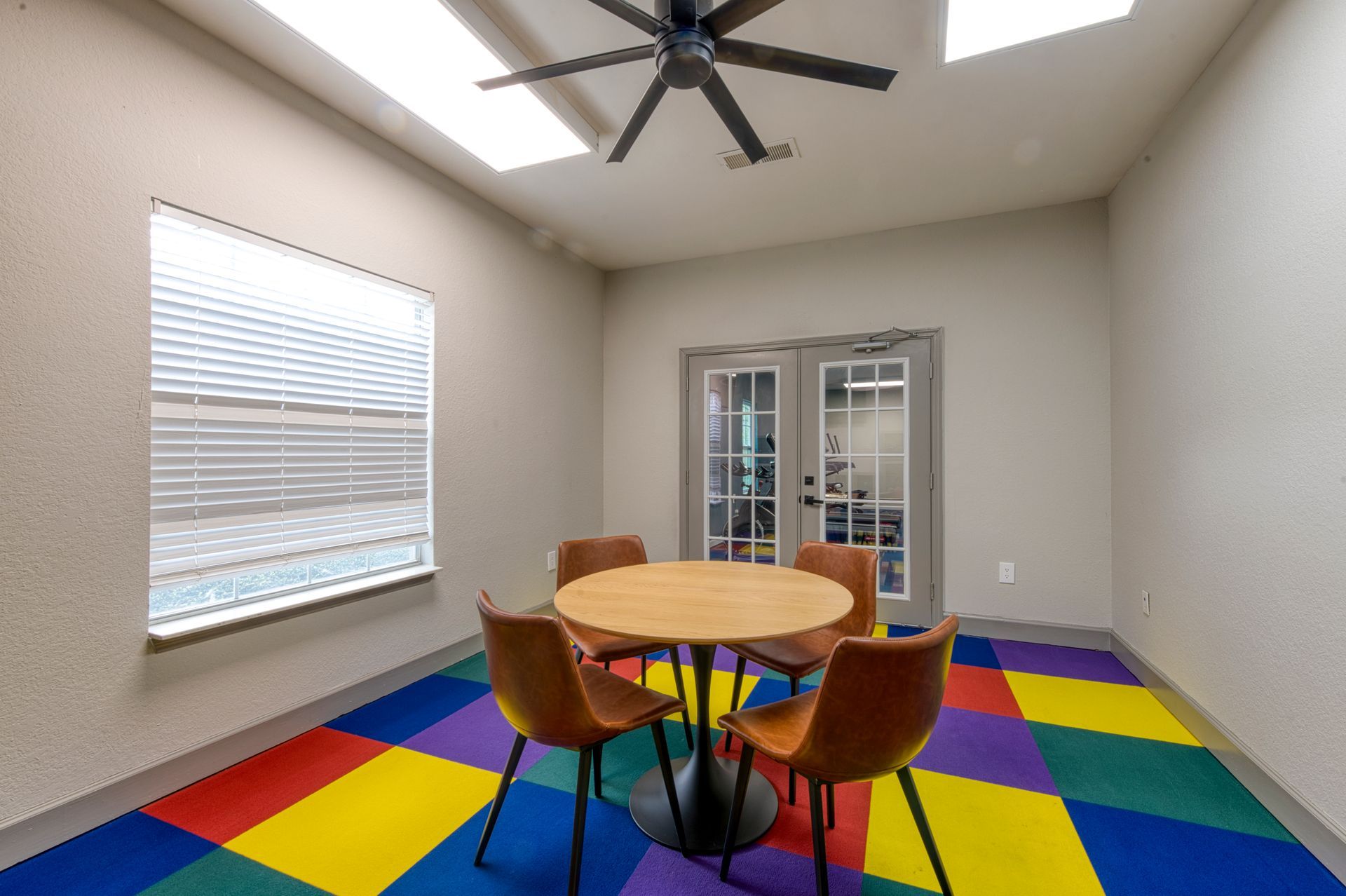 Bright meeting room with a round table, four chairs, and a colorful tiled floor.