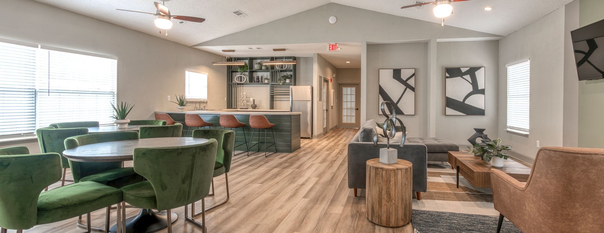 Modern apartment lounge with green chairs, bar seating, sofas, and wood flooring