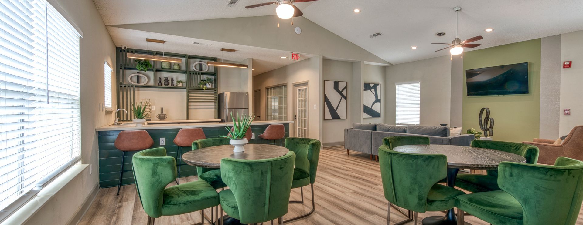 Modern dining room with green velvet chairs, round tables, bar seating, and large windows