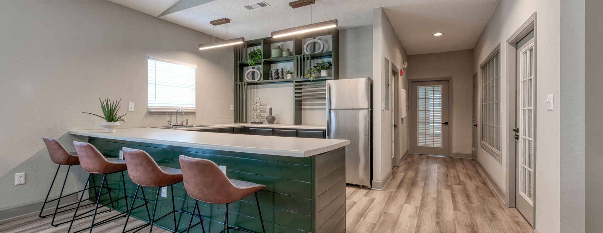 Modern kitchen with island bar, pink stools, stainless appliances, and hallway leading to bedrooms
