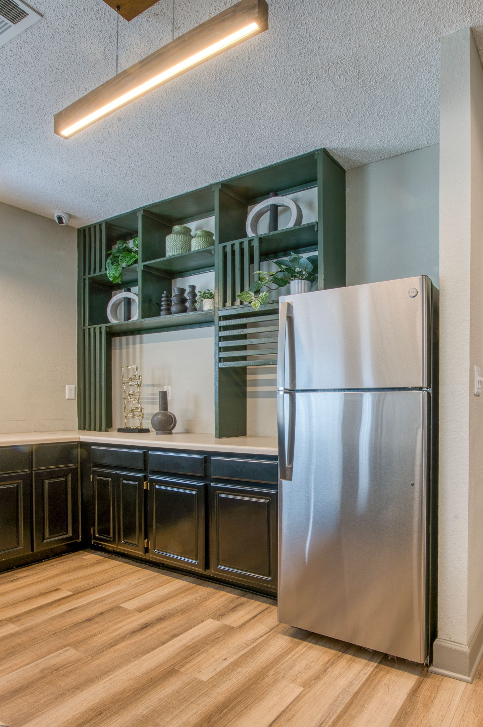 Modern kitchen with green open shelving, black cabinets, and a stainless steel refrigerator.