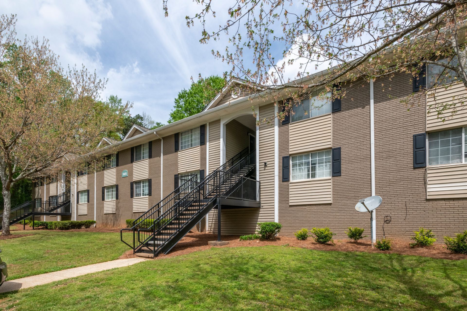 Apartment building exterior with brick facade, stairs, and landscaped lawn