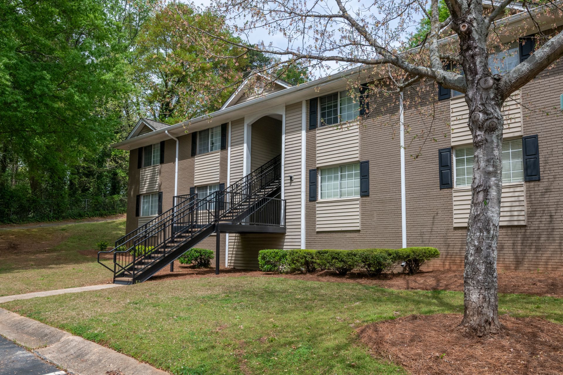 Suburban apartment building with tan siding, black stairs, and a tree in front