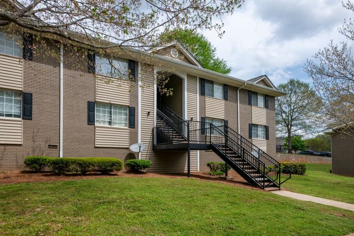 Apartment building exterior with beige siding, black stairs, and a grassy lawn
