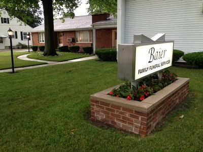 Apartment complex sign reading “River” beside brick buildings and a landscaped lawn