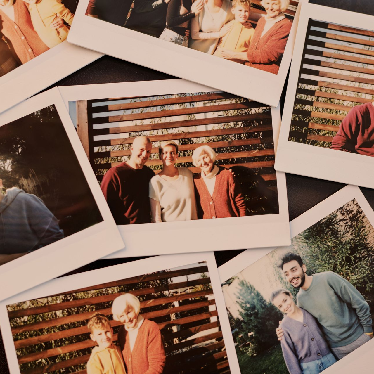 Scattered printed photos showing smiling people posing outdoors and indoors on a wooden backdrop