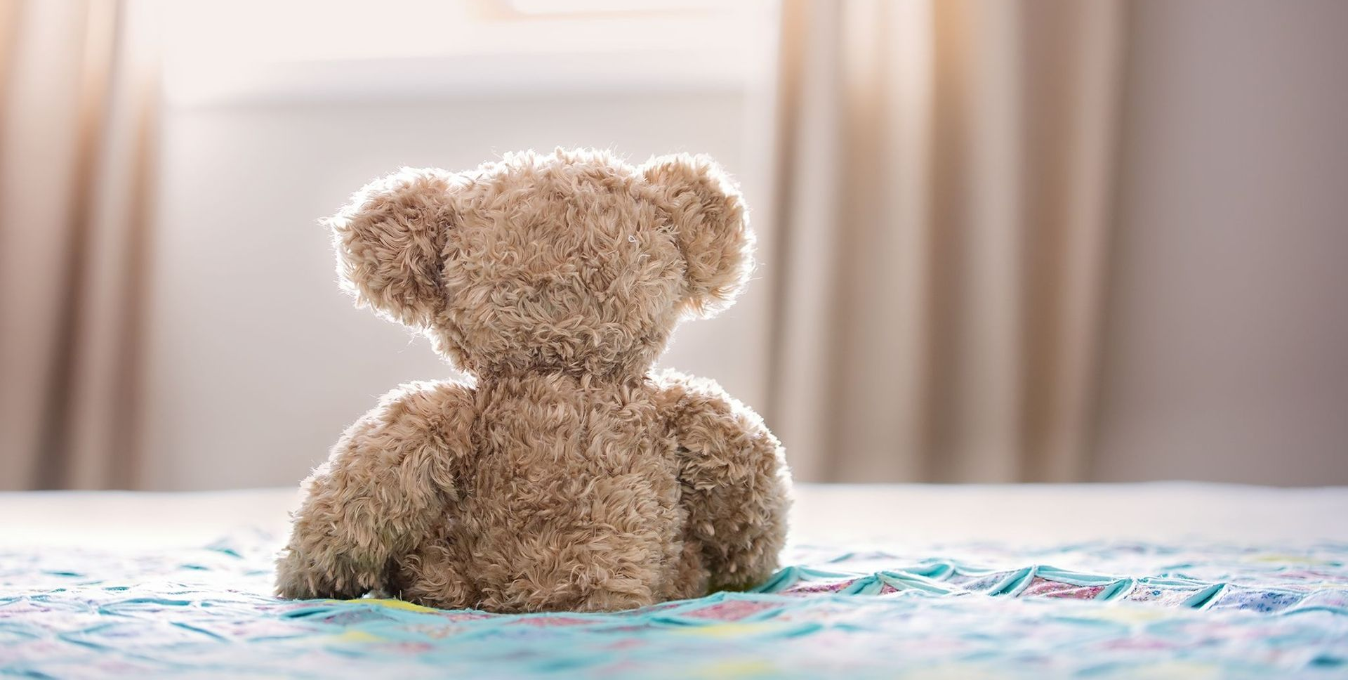 Fluffy teddy bear sitting on a bed with soft curtains in the background