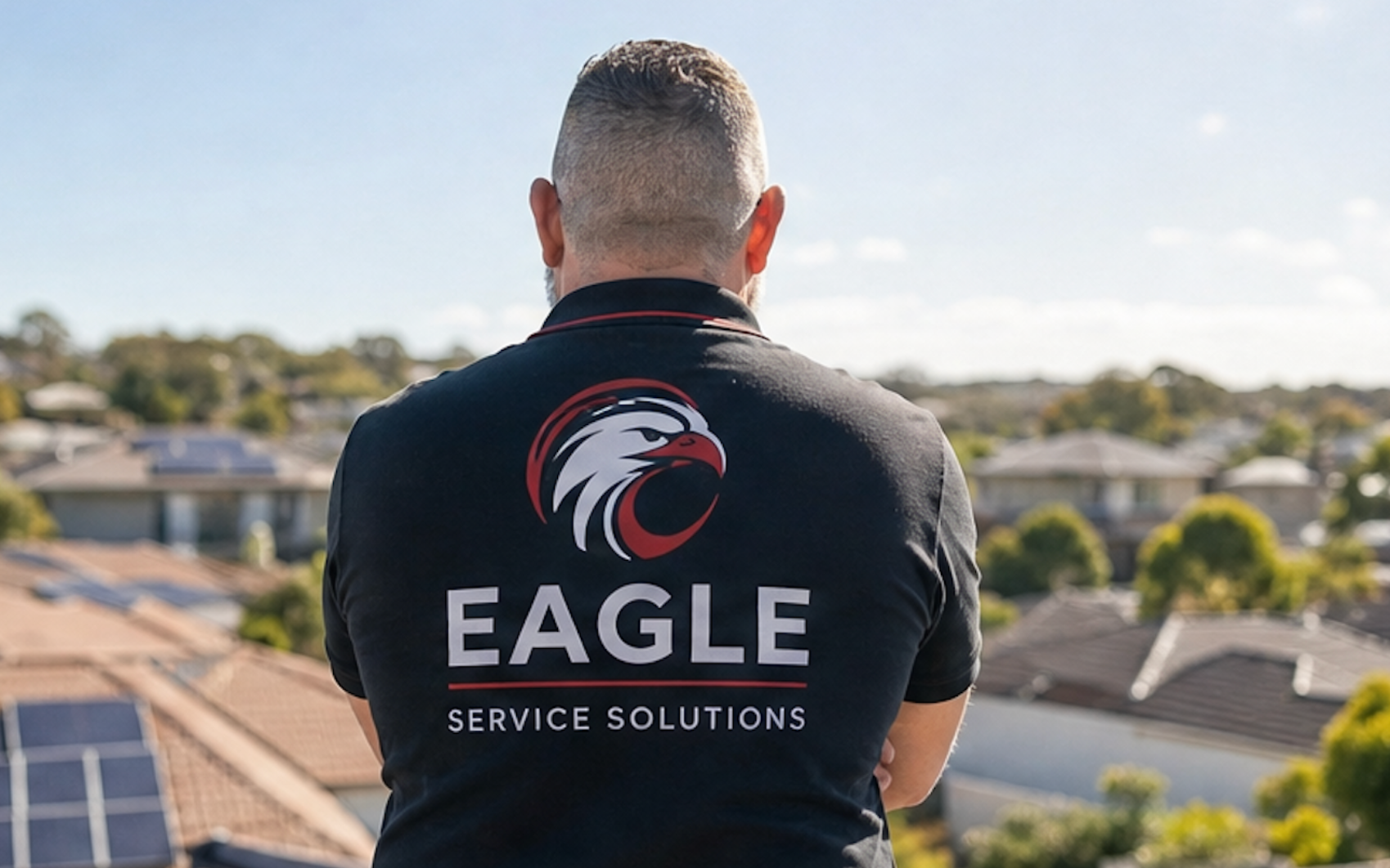 Person in black EAGLE Service Solutions jacket overlooking a suburban neighborhood at sunset