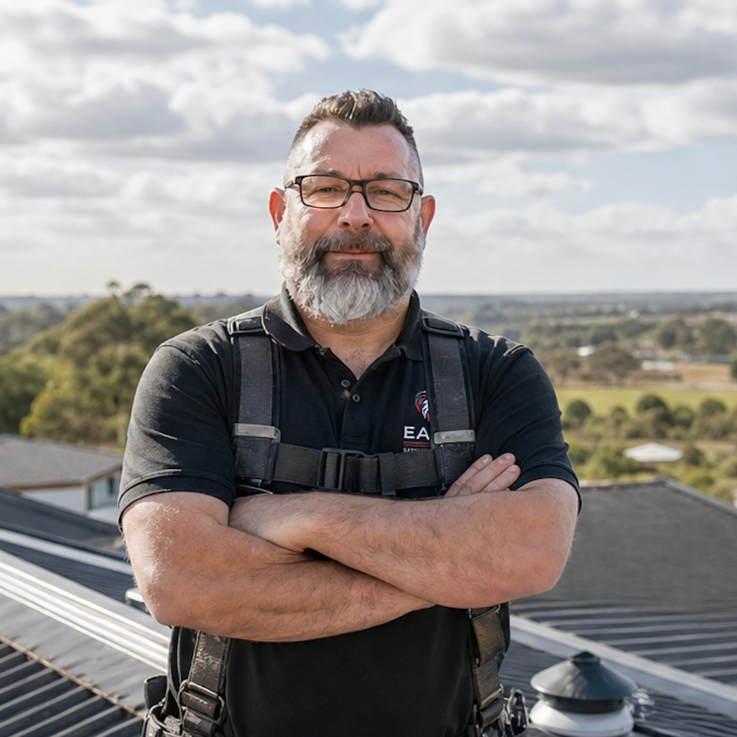 Man standing with arms crossed on a rooftop, wearing a black shirt and overalls, with a cloudy landscape behind him