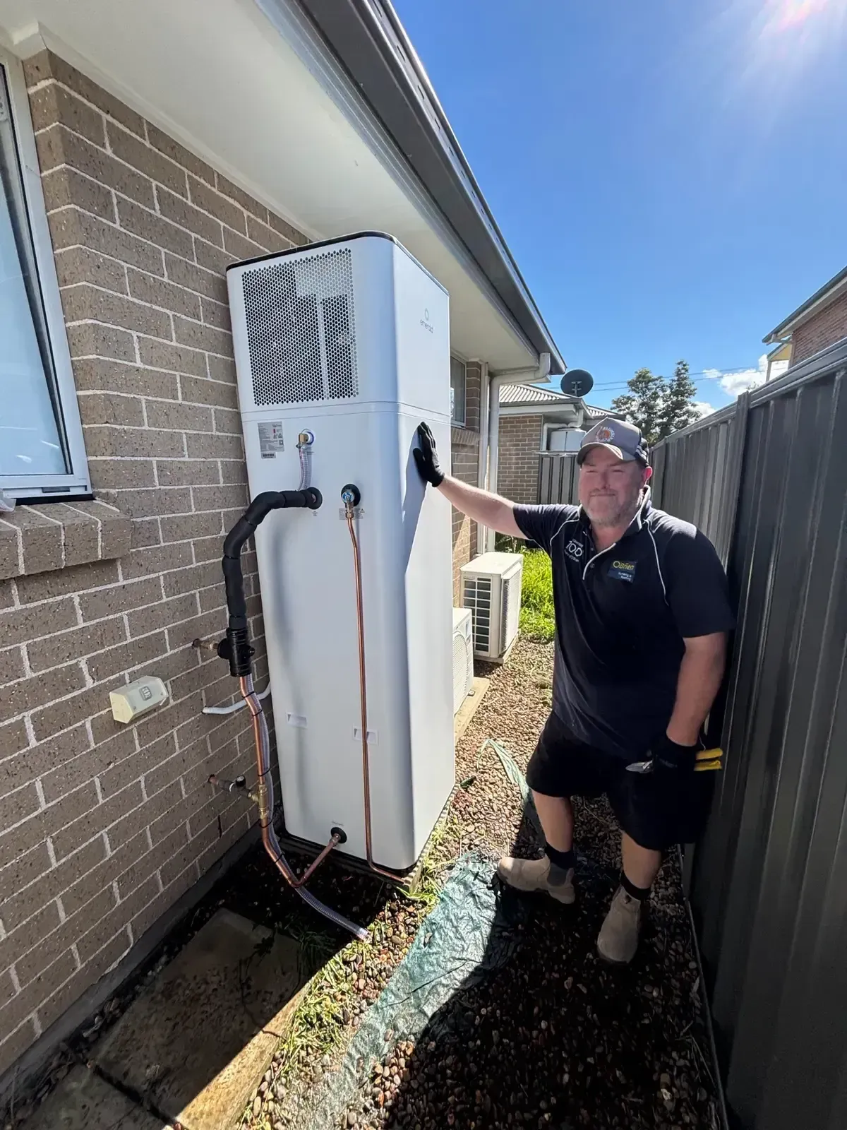 Technician inspecting a white outdoor unit beside a brick house in a narrow side yard
