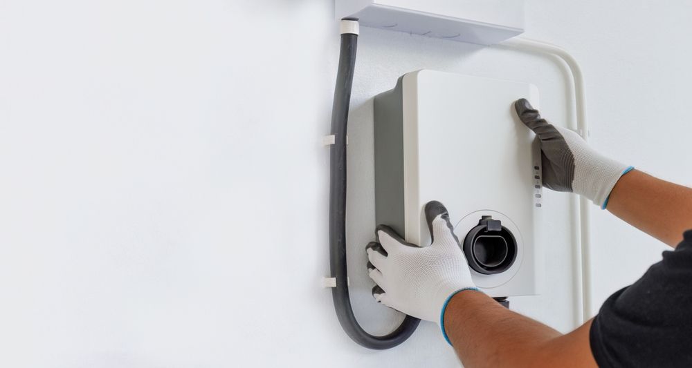 Person wearing gloves adjusts a wall-mounted electrical panel with cables attached