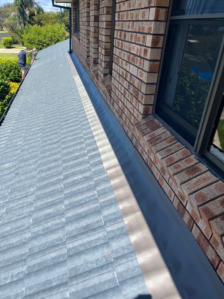 Corrugated metal roof beside a brick house wall and window, viewed from above