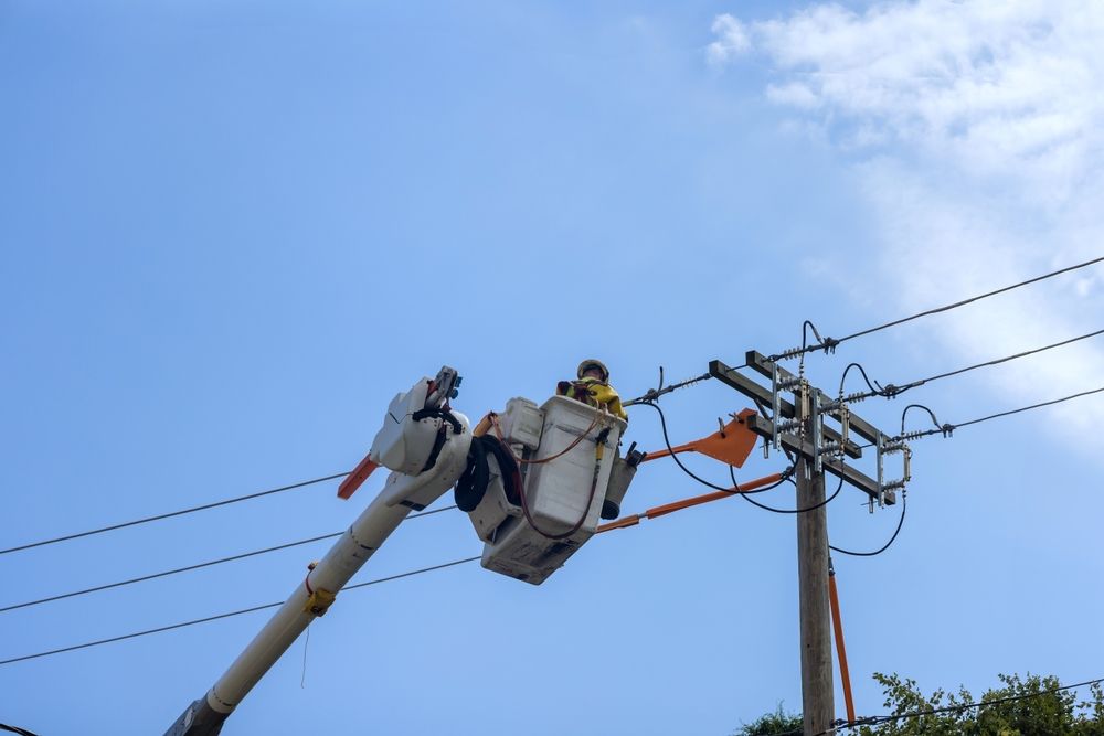 Utility workers in a bucket truck repairing power lines against a blue sky