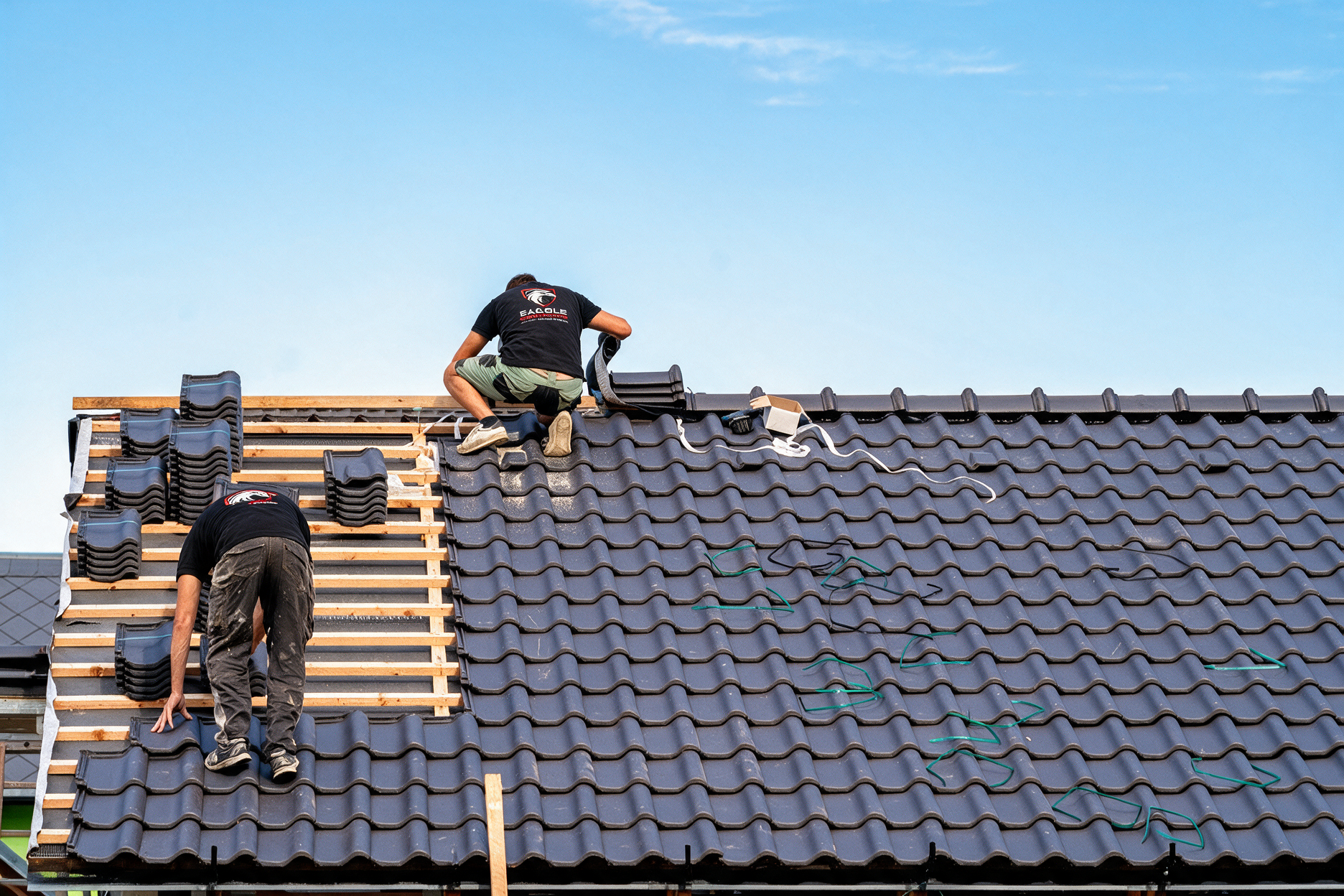 Workers installing roof tiles on a house under a clear blue sky