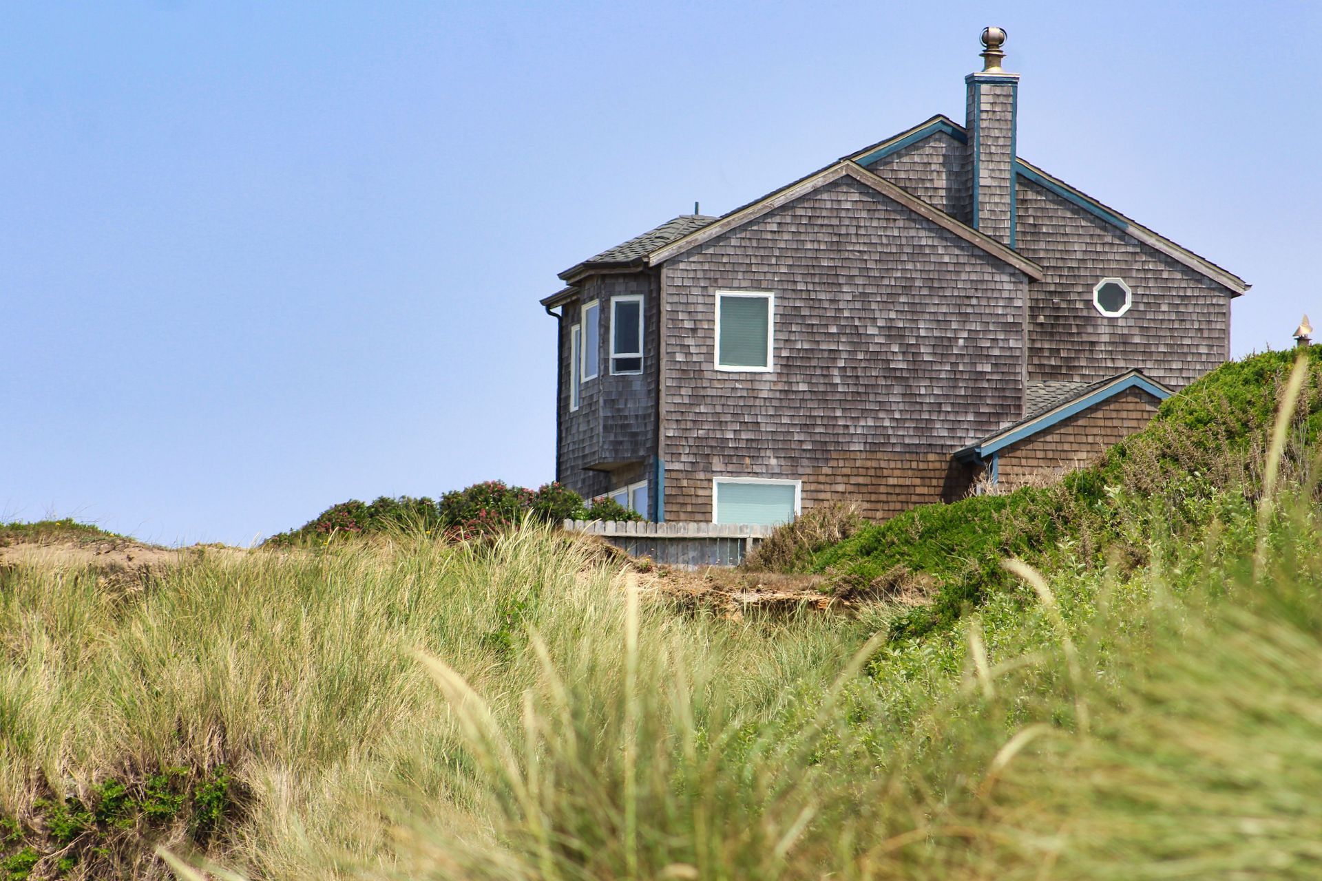 Weathered seaside house behind tall dune grass under a clear sky