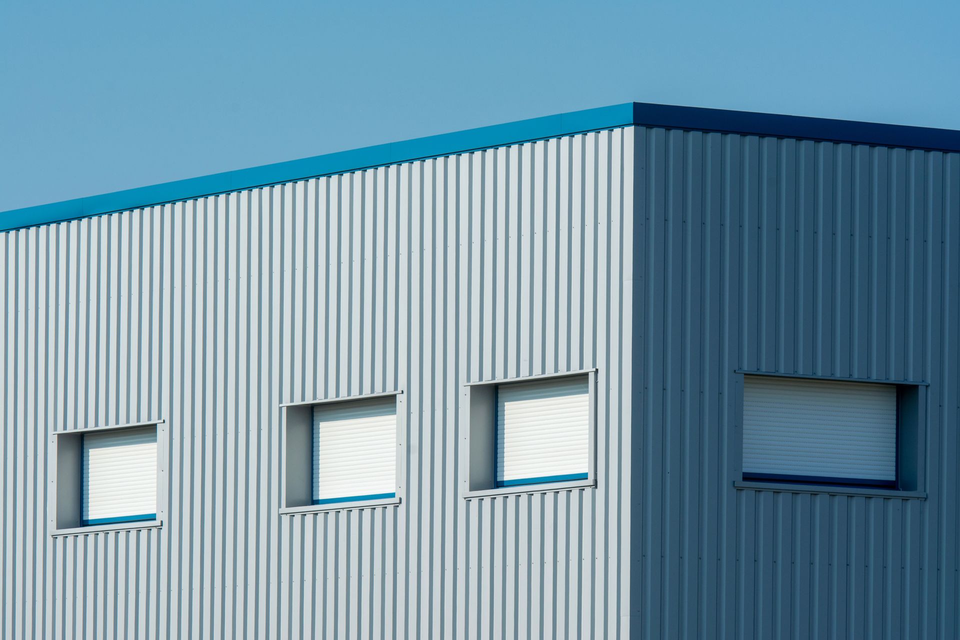 Modern industrial building corner with blue trim and small windows against a clear sky