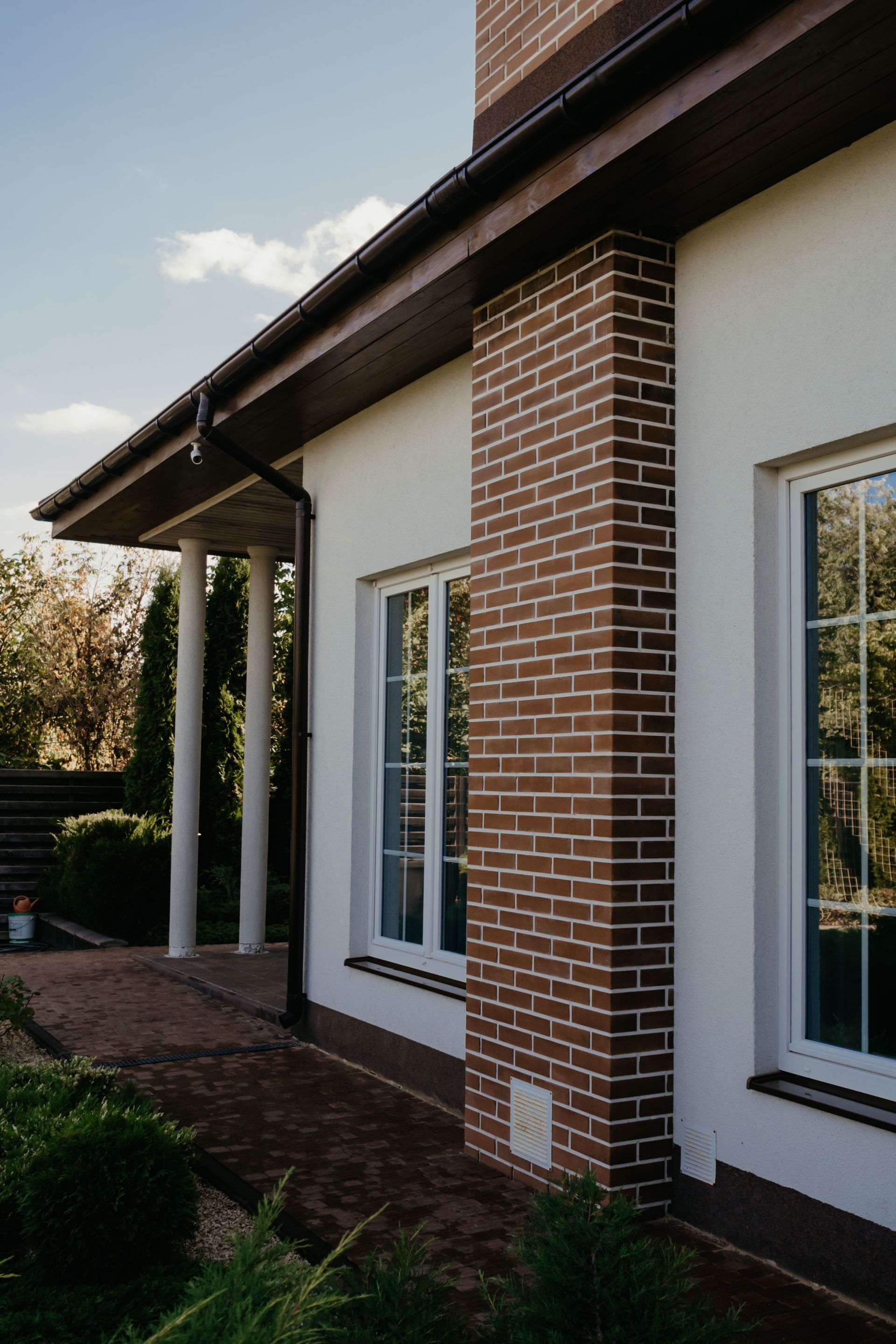 Exterior of a house with white walls, brick columns, and windows under a covered roof