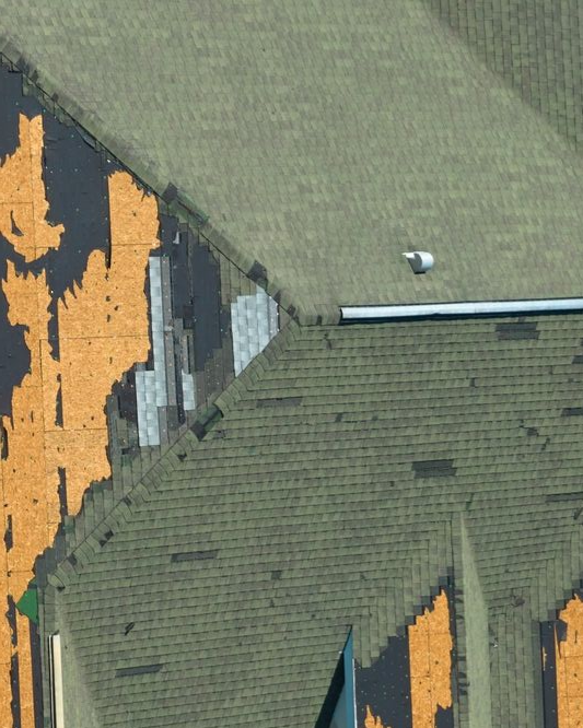 Aerial view of damaged roof with missing shingles and exposed patches