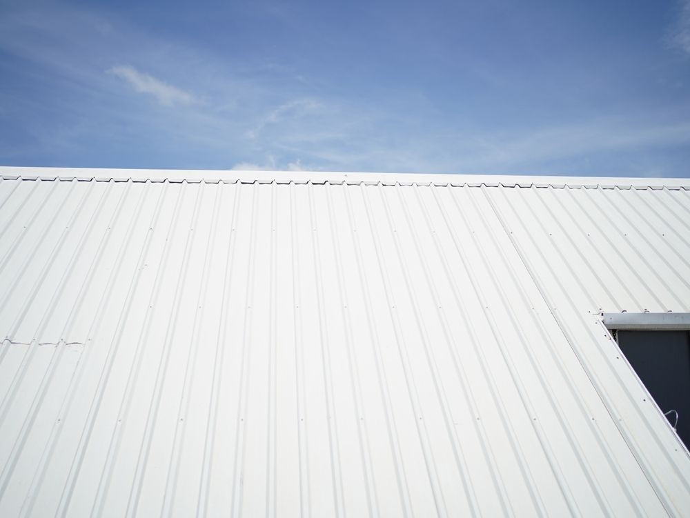 White corrugated metal roof under a blue sky, with a small doorway at the right edge