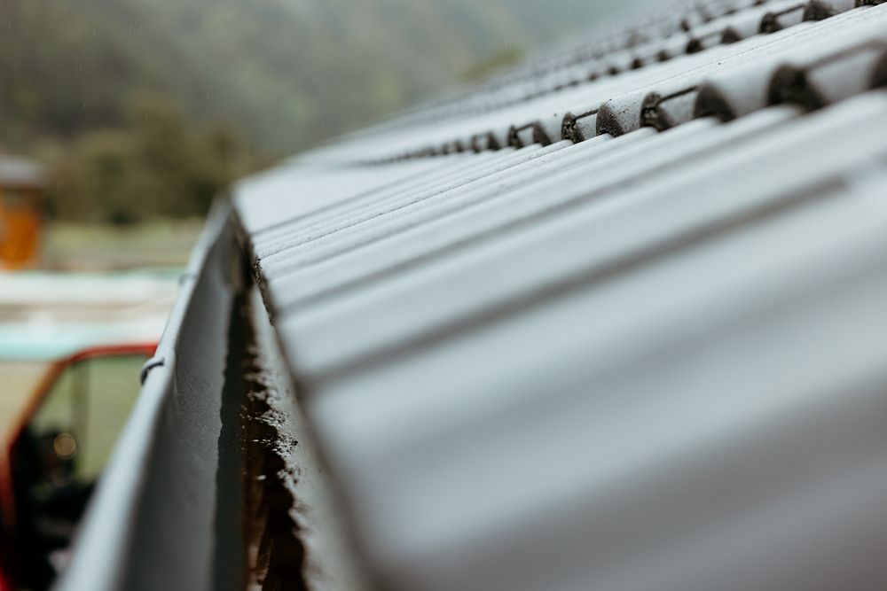Close-up of a gray corrugated metal roof edge with blurred background and orange vehicle in the distance