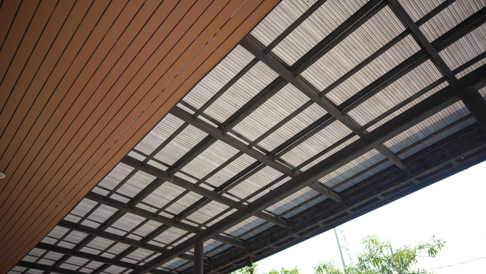 Underside of a modern roof with wood slats and metal beams against the sky and trees