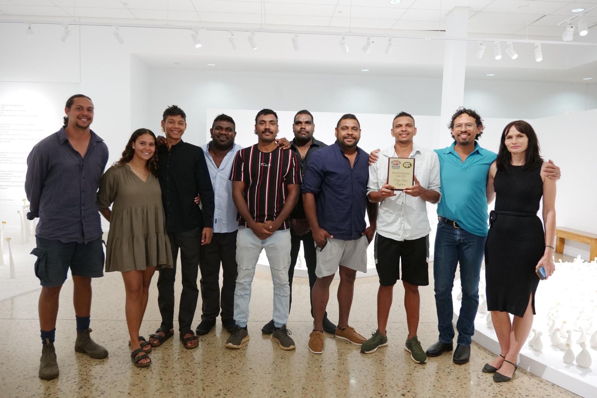 Group of people in an art gallery holding an award. Diverse group smiling. White room setting.
