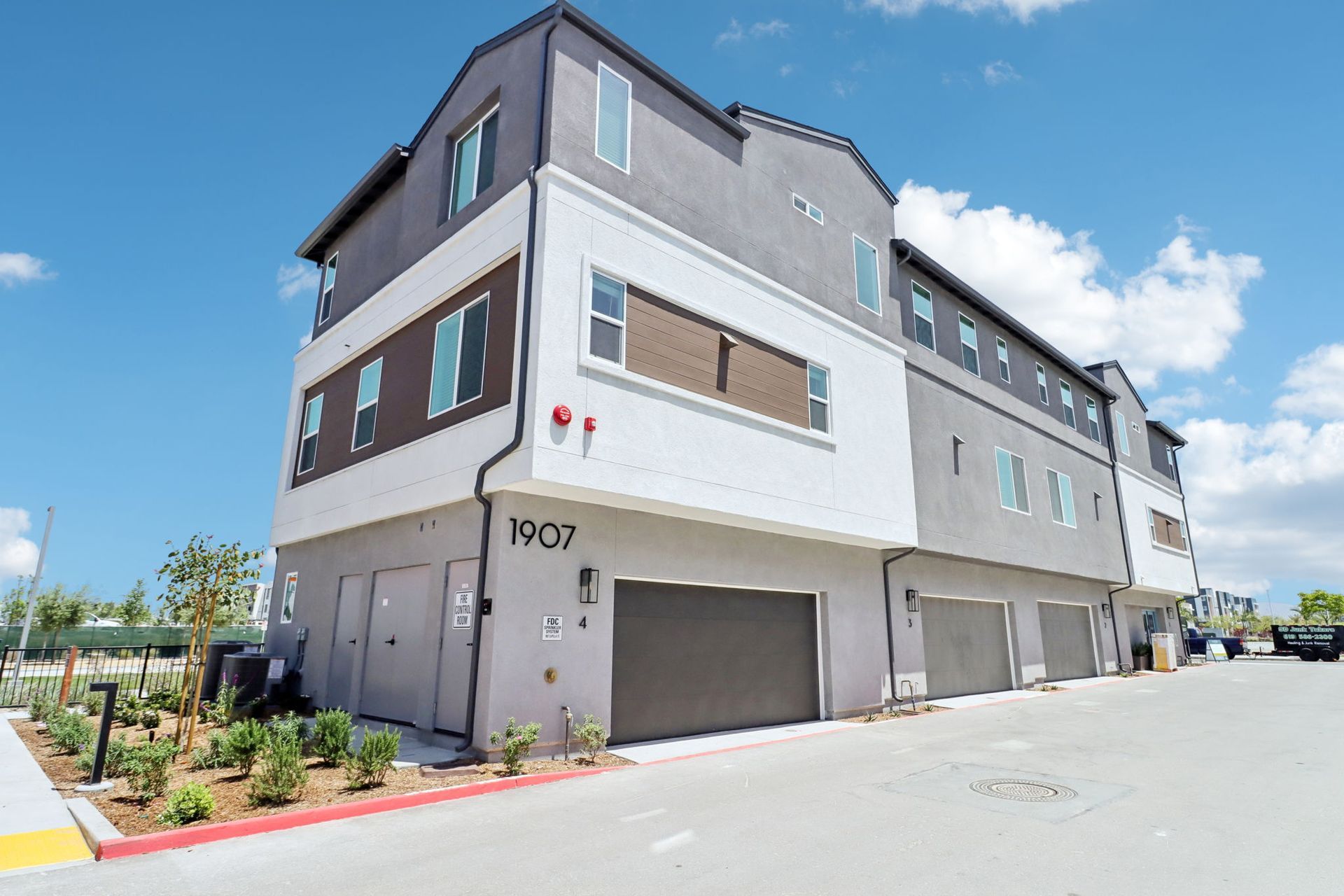 Three-story townhomes with gray and white exterior, gray garage doors, blue sky.