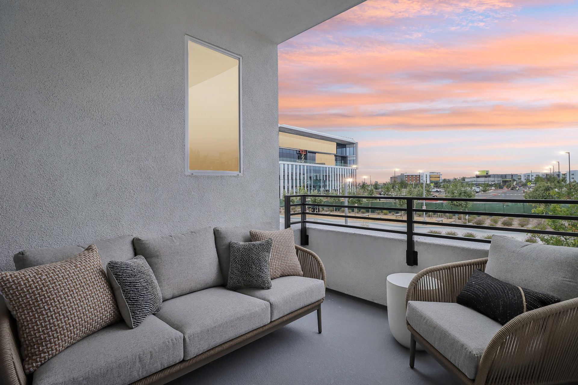Balcony with outdoor sofa, pillows, and sunset view over buildings.