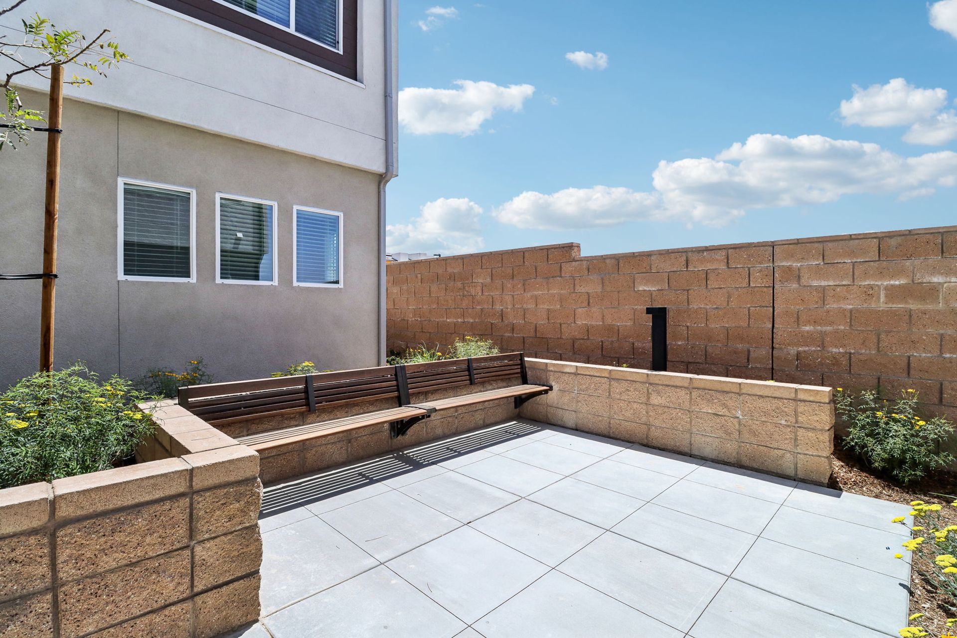 Back patio with a concrete floor, brick walls, bench, and a clear blue sky.