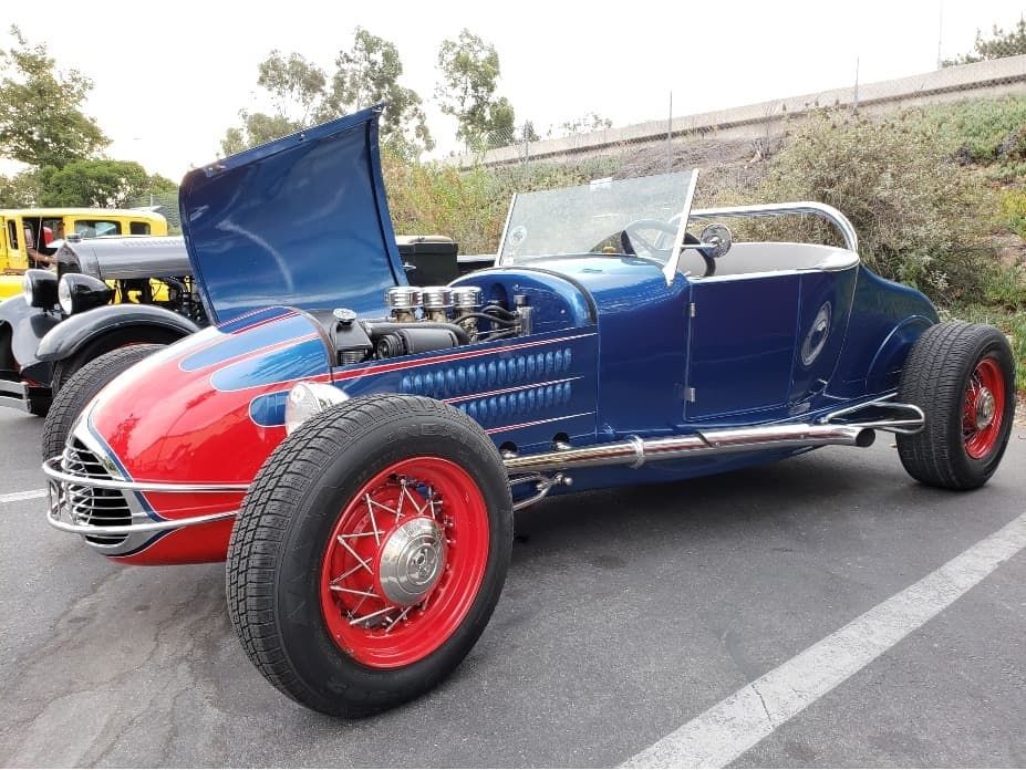 Blue and red classic hot rod with hood open, parked outdoors.