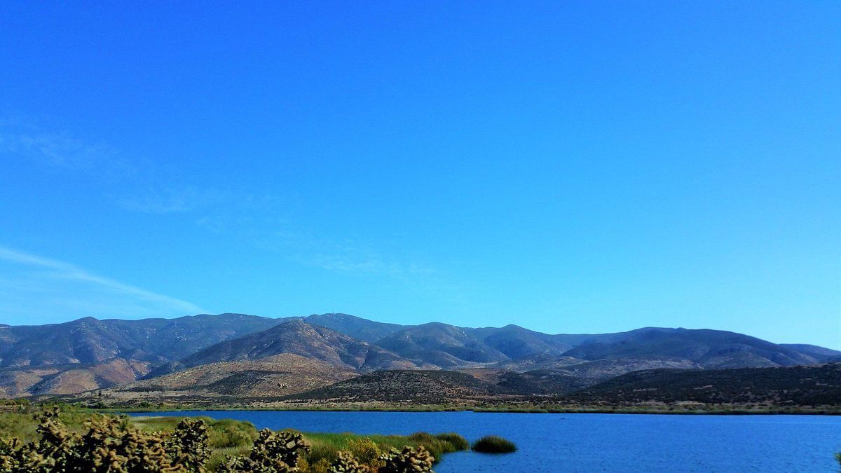 Blue lake with mountains under a clear blue sky.