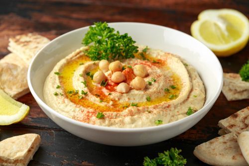 Bowl of hummus garnished with chickpeas, parsley, and paprika, served with pita bread and lemon slices.