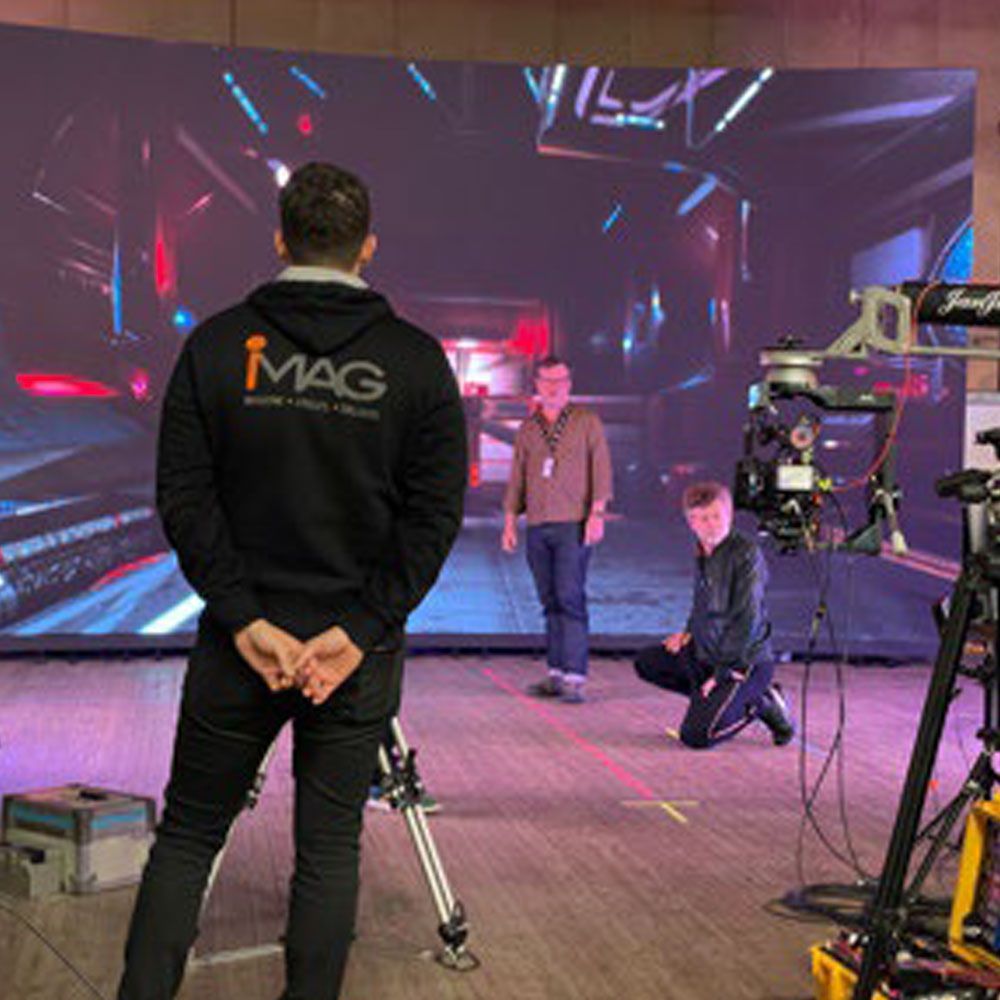 A man wearing a black hoodie stands in front of a large screen