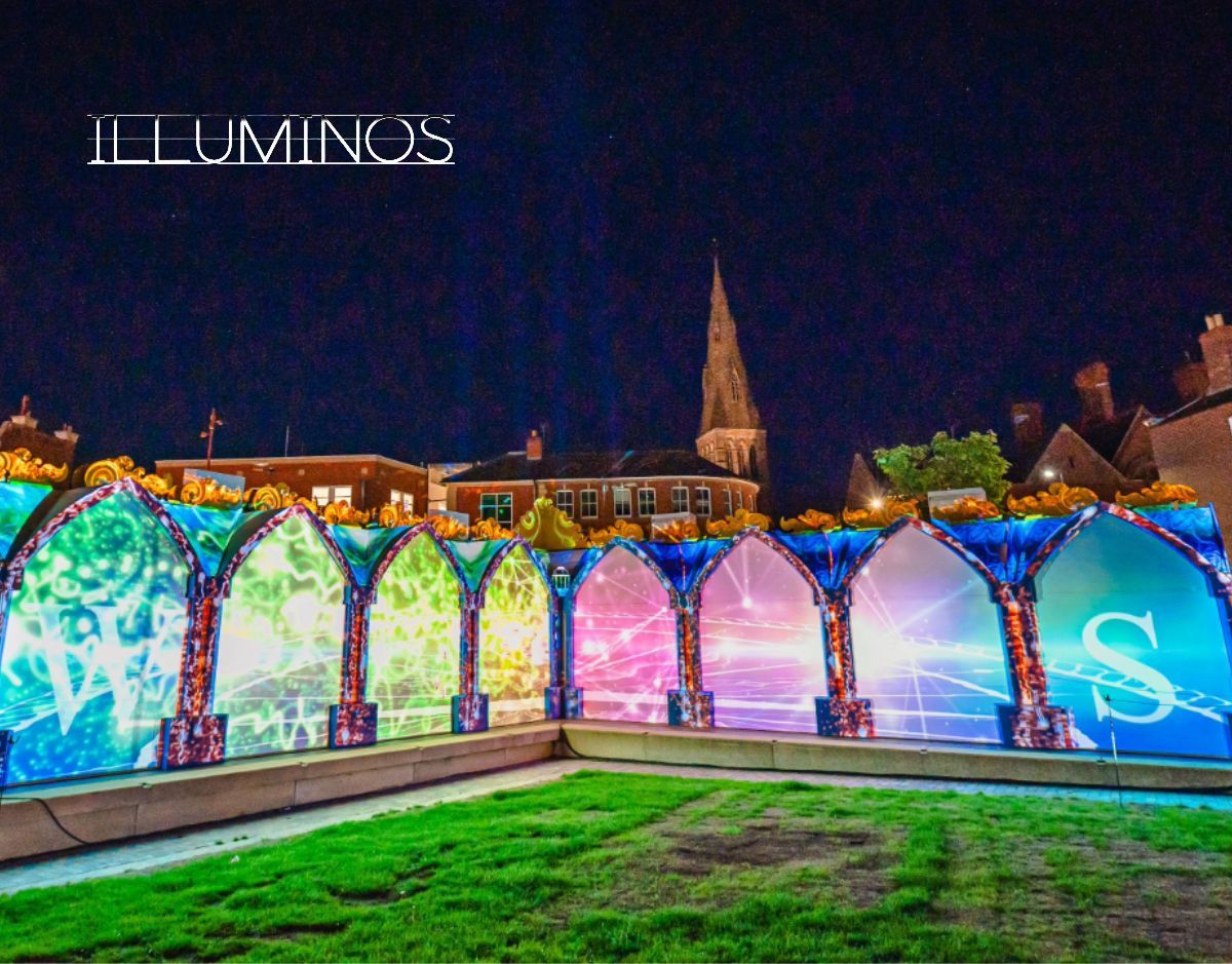 Illuminos light display on arched wall at night, glowing in rainbow colors over a grassy foreground