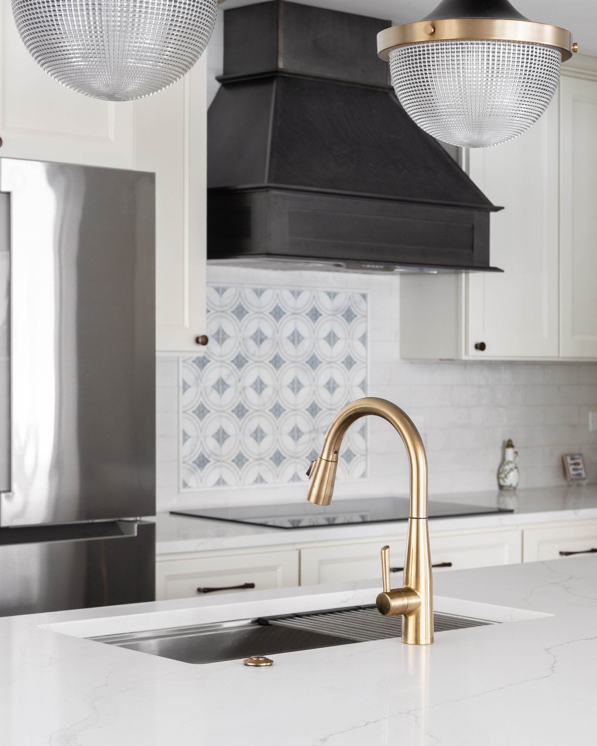 Modern kitchen with white cabinets, black range hood, gold faucet, and white marble island