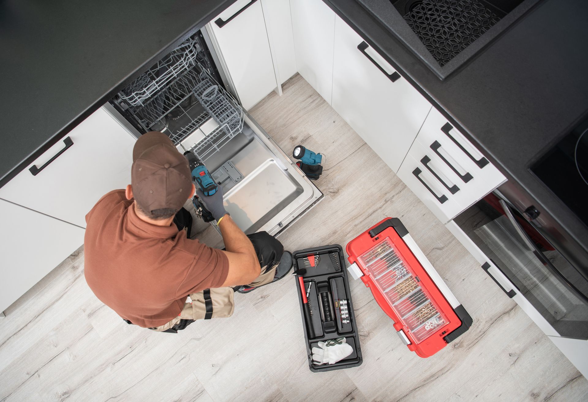 Technician kneels by an open server rack, working with tools and parts in a white equipment room.