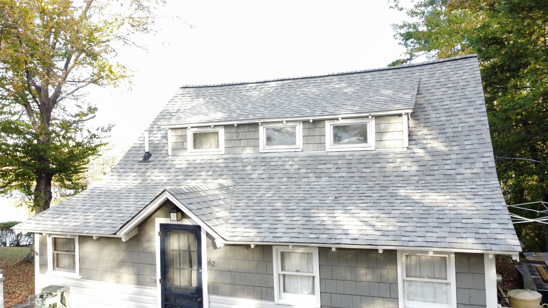 Gray house with steep shingled roof, front porch, and dormer windows in a leafy yard Gray house with steep shingled roof, front porch, and dormer windows in a leafy yard