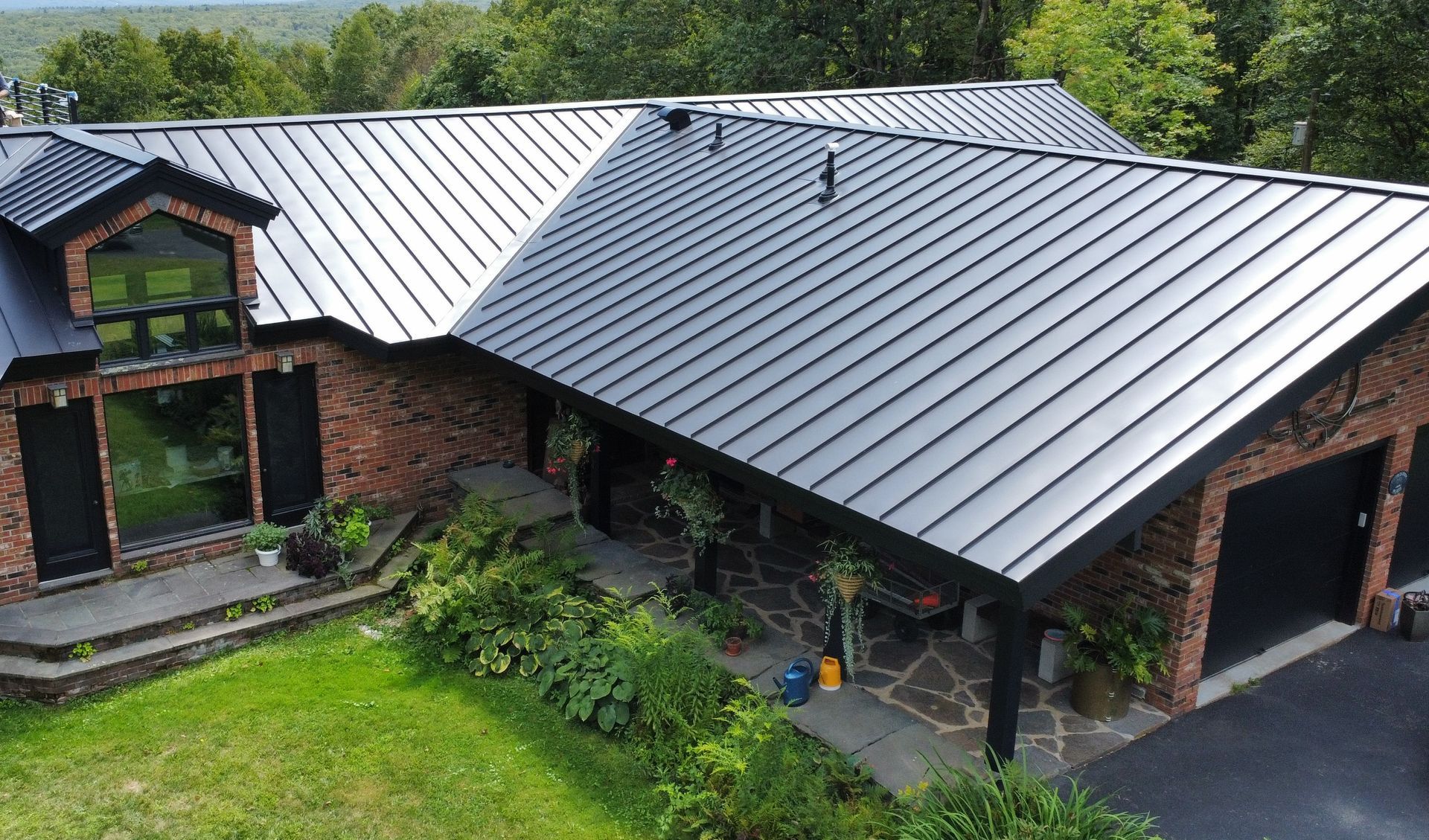 Modern brick house with gray metal roof, front entry, and attached garage amid green lawn. Modern brick house with gray metal roof, front entry, and attached garage amid green lawn.