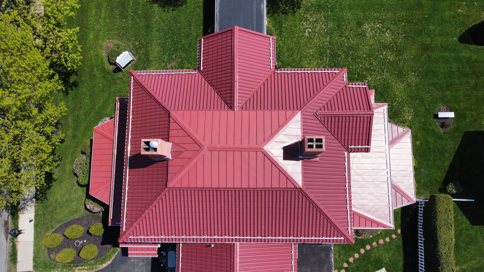 An aerial view of a large house with a red metal roof and chimneys. ATAS Techo Tile metal roof on Mitchells Funeral Home in Easthampton MA