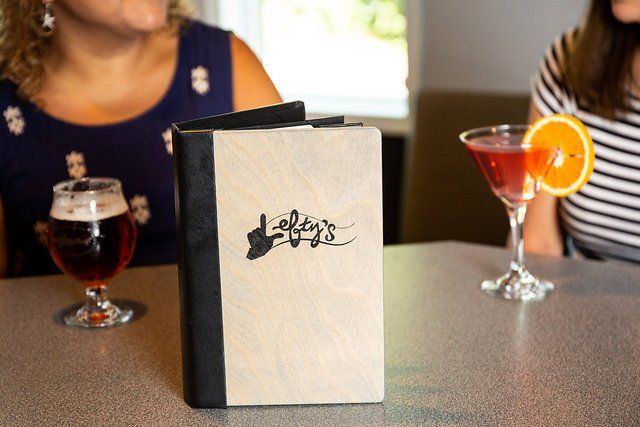 Two women are sitting at a table with drinks and a menu.