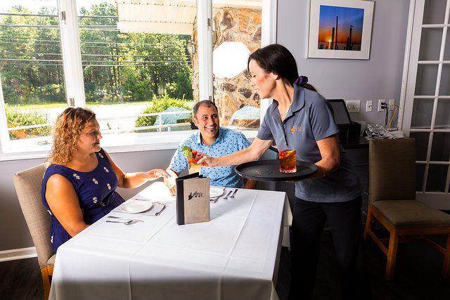A woman is serving a drink to two people sitting at a table in a restaurant.