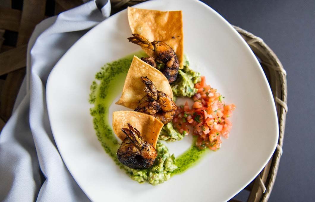 A white plate topped with shrimp , guacamole and salsa.