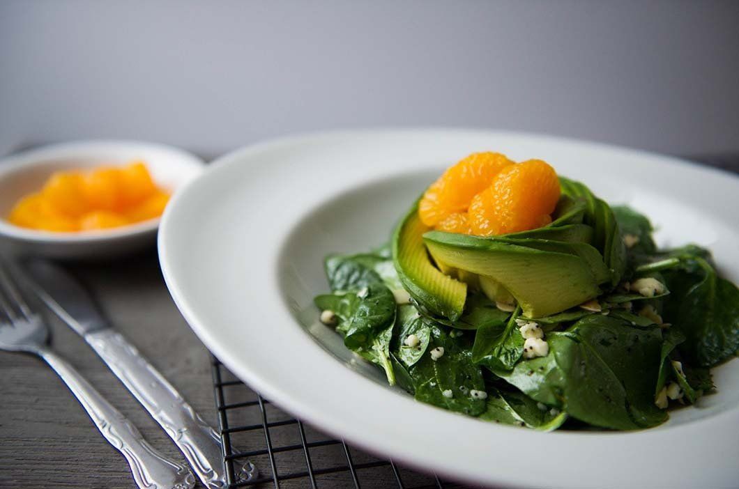A white plate topped with a salad of spinach , zucchini and oranges.