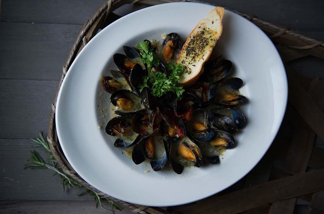 A white plate topped with mussels and a piece of garlic bread.