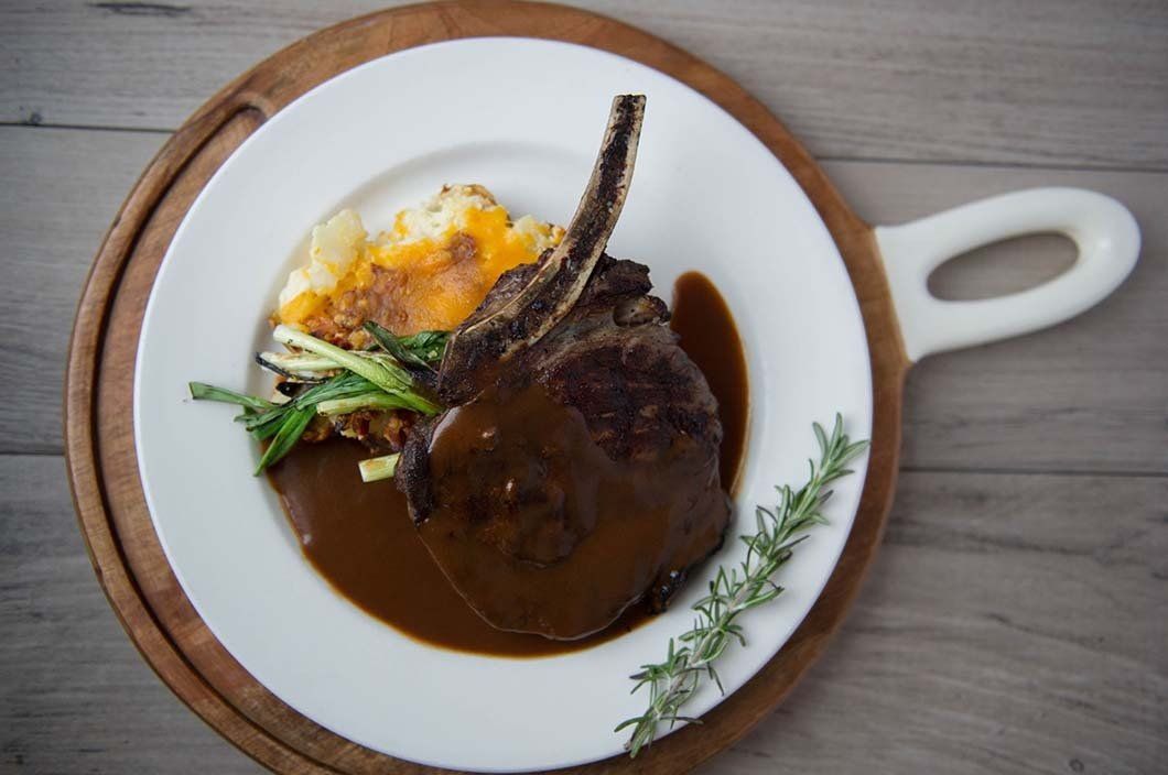 A white plate topped with meat and mashed potatoes on a wooden cutting board.